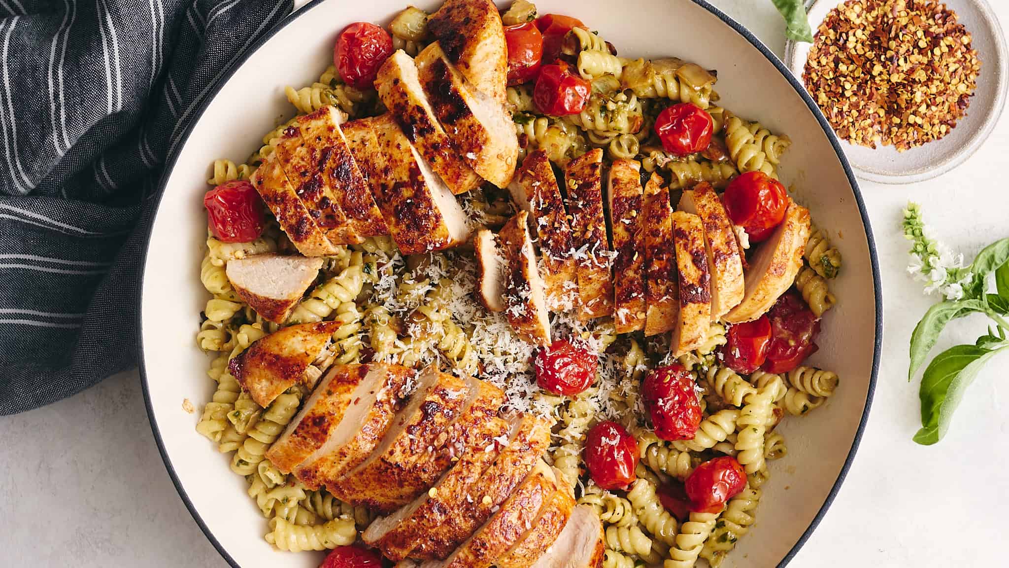 Succulent grilled chicken breast slices served over a pasta salad with cherry tomatoes, shredded cheese, and herbs, garnished for a flavorful dinner.