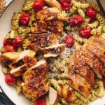 Grilled chicken pasta salad with cherry tomatoes, basil, and grated cheese in a white serving dish. Fresh ingredients and herbs are visible, creating an appetizing and colorful presentation.