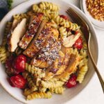 Sliced grilled chicken served over pasta with cherry tomatoes and herbs, garnished with shredded cheese in a rustic bowl for a delicious and healthy meal.