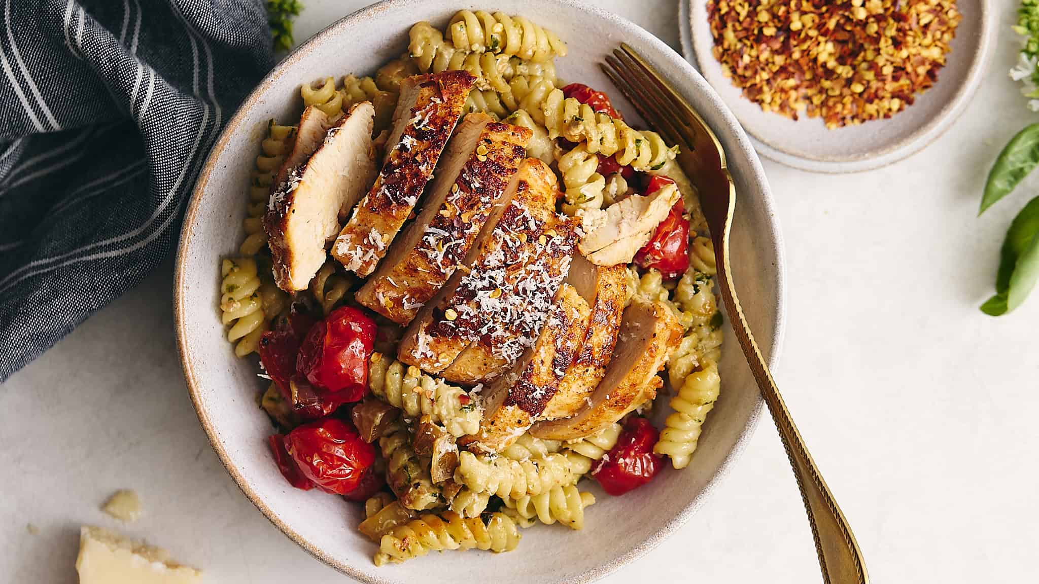 Sliced grilled chicken served over pasta with cherry tomatoes and herbs, garnished with shredded cheese in a rustic bowl for a delicious and healthy meal.