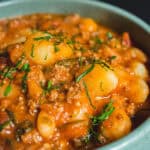 Creamy potato and minced meat stew garnished with fresh herbs in a teal bowl, showcasing a hearty, flavorful comfort food perfect for dinner.