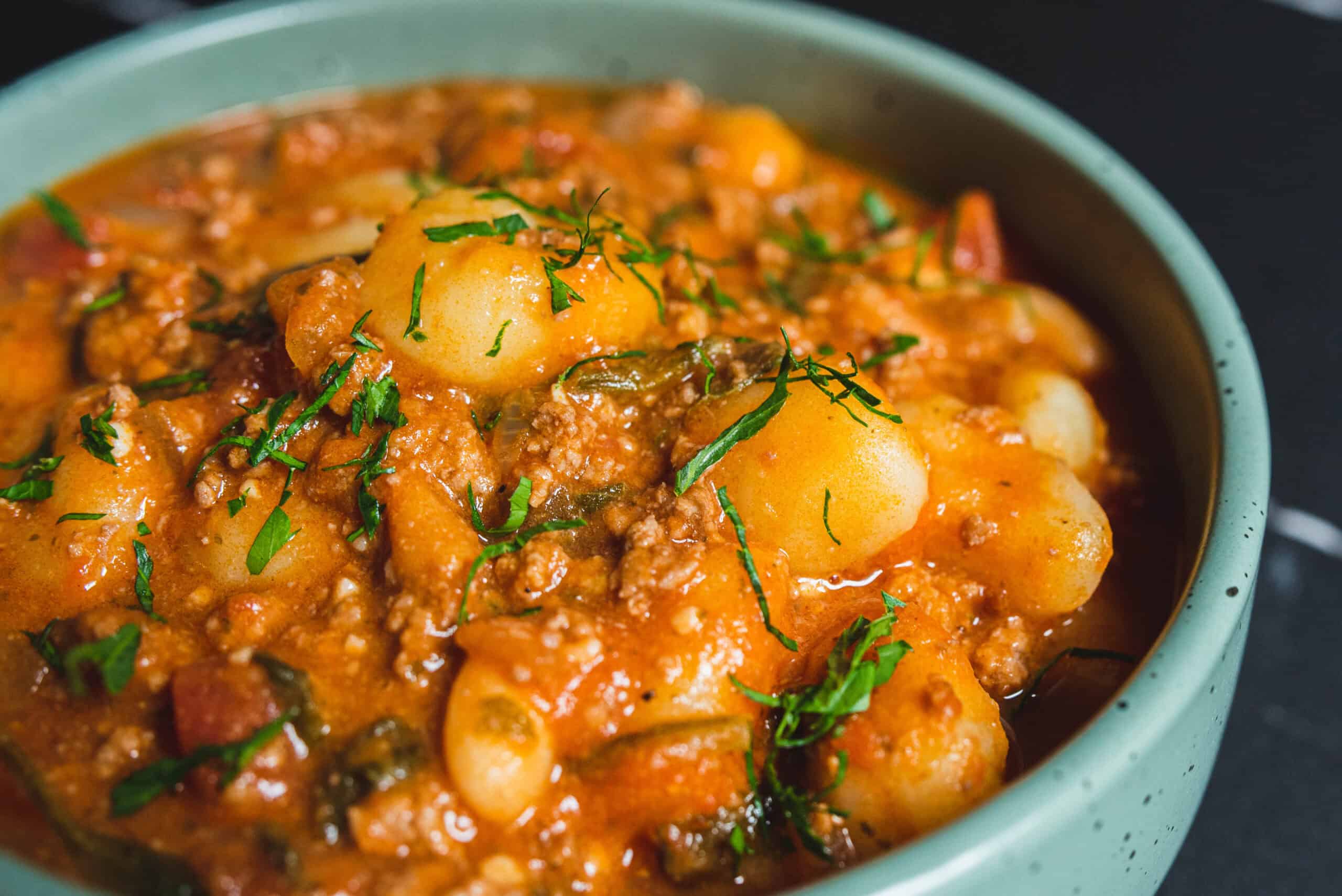 Creamy potato and minced meat stew garnished with fresh herbs in a teal bowl, showcasing a hearty, flavorful comfort food perfect for dinner.