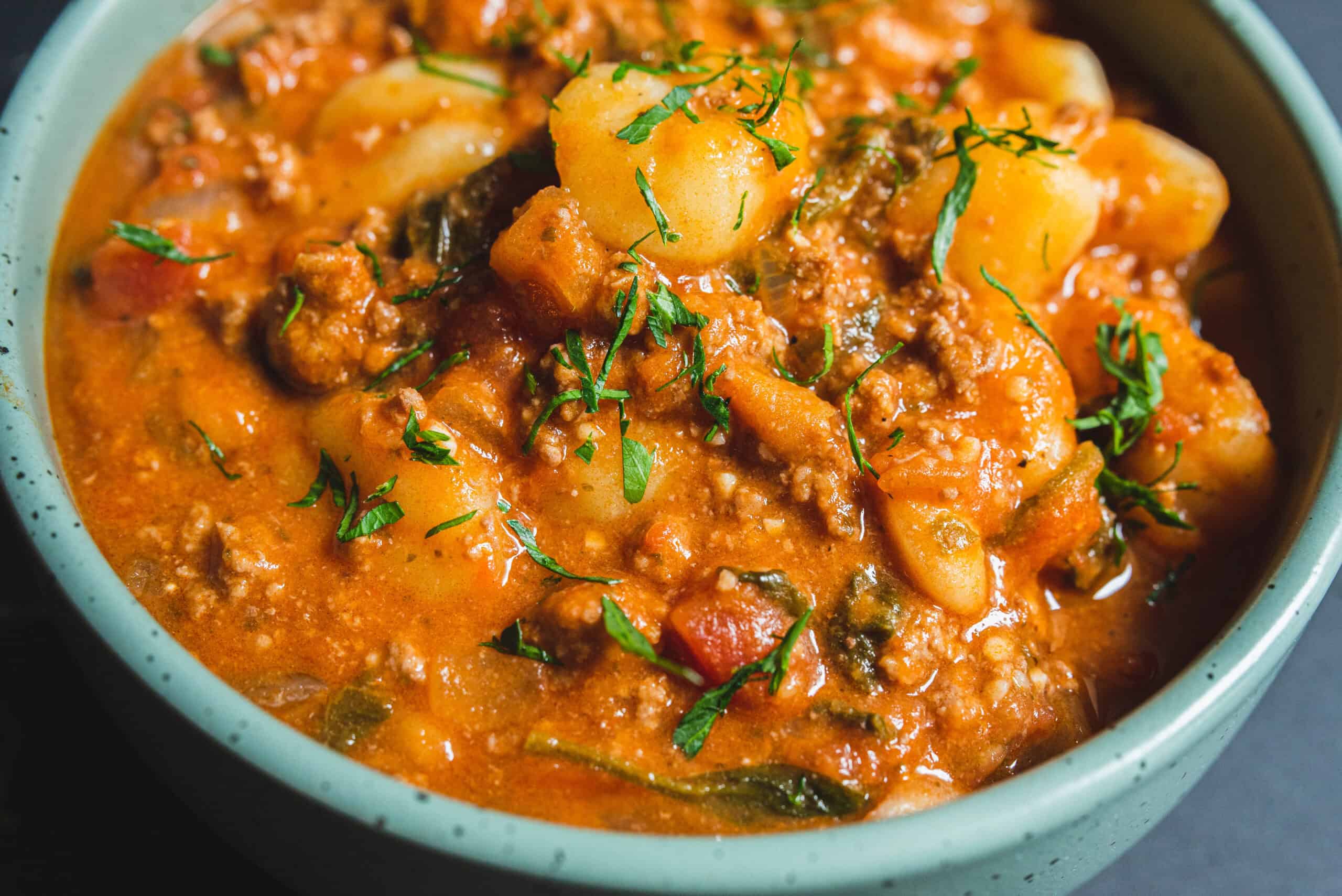 Creamy potato and ground beef curry garnished with fresh herbs in a bowl, featuring a rich, flavorful sauce packed with vegetables and spices. Perfect for hearty Indian-inspired meals.