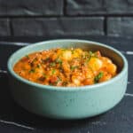 Creamy beef and potato stew garnished with fresh herbs in a light green bowl on a dark textured surface.