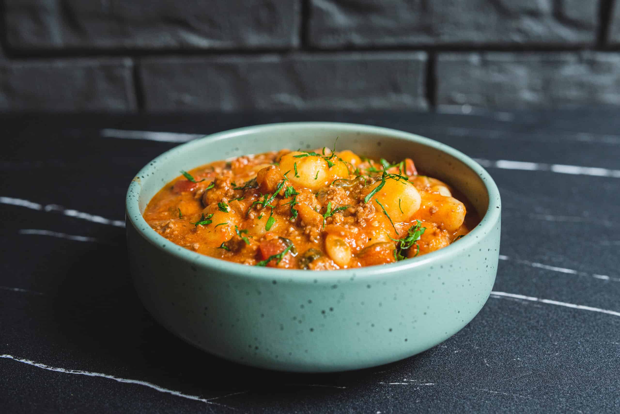Creamy beef and potato stew garnished with fresh herbs in a light green bowl on a dark textured surface.