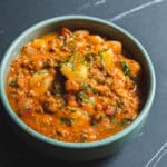 Savory Indian vegetable curry served in a light blue bowl, garnished with fresh cilantro, on a dark marble surface.