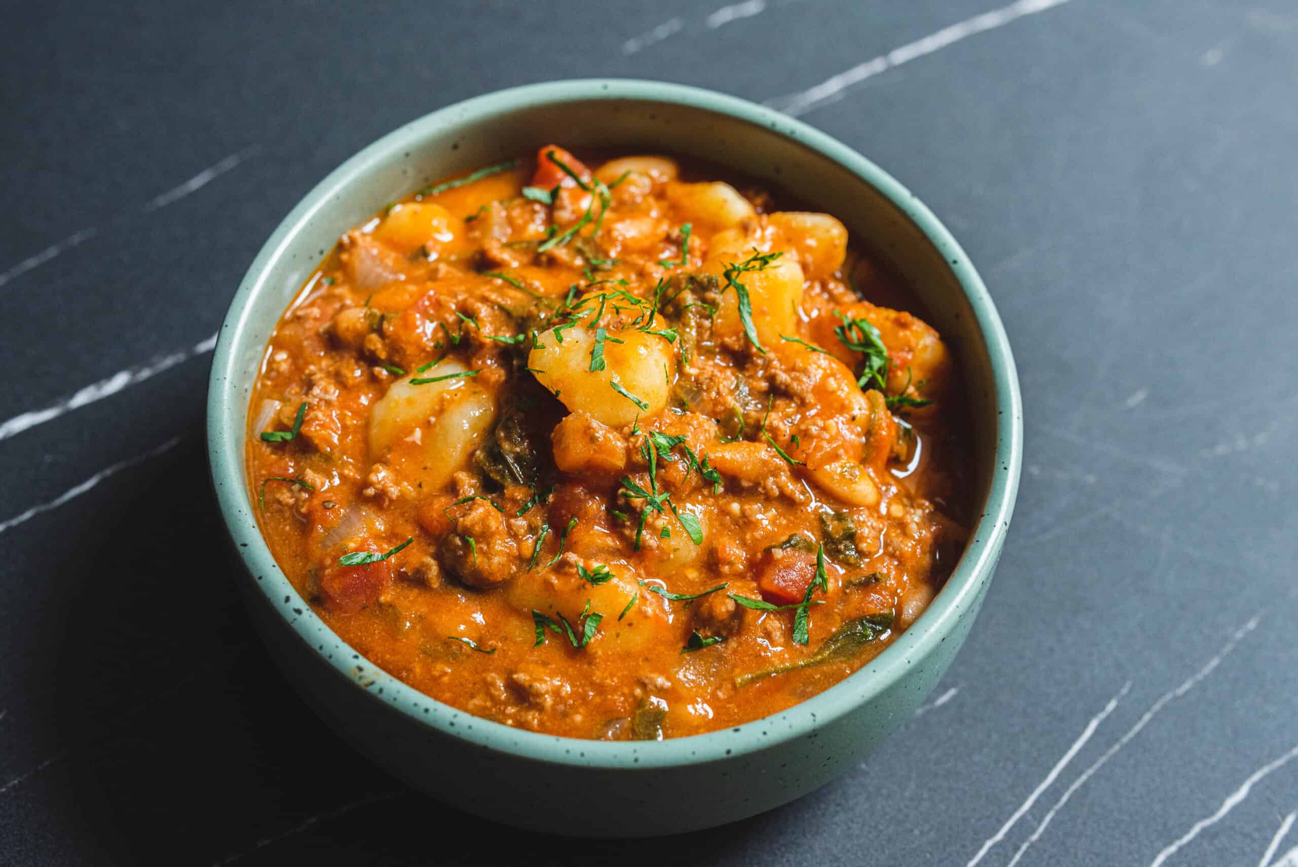 Savory Indian vegetable curry served in a light blue bowl, garnished with fresh cilantro, on a dark marble surface.