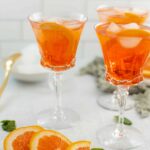 Bright orange citrus drinks served in elegant cocktail glasses with ice and orange slices, perfect for summer or brunch gatherings.