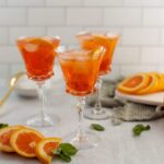 Bright orange citrus cocktail with ice served in elegant crystal glasses, garnished with fresh orange slices and mint leaves, ideal for summer drinks and entertaining.
