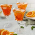 Fruity orange cocktail served in elegant crystal glasses with ice and orange slices, perfect for summer refreshment. Garnished with fresh oranges and mint leaves for a vibrant, citrus-themed presentation.