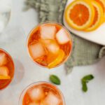 Refreshing orange iced tea with lemon slices and ice cubes, served in clear glasses, perfect for summer beverages and citrus-infused drinks.
