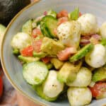 Fresh tomato, cucumber, and mozzarella salad with avocado and herbs in a ceramic bowl, perfect for healthy eating and summer recipes.