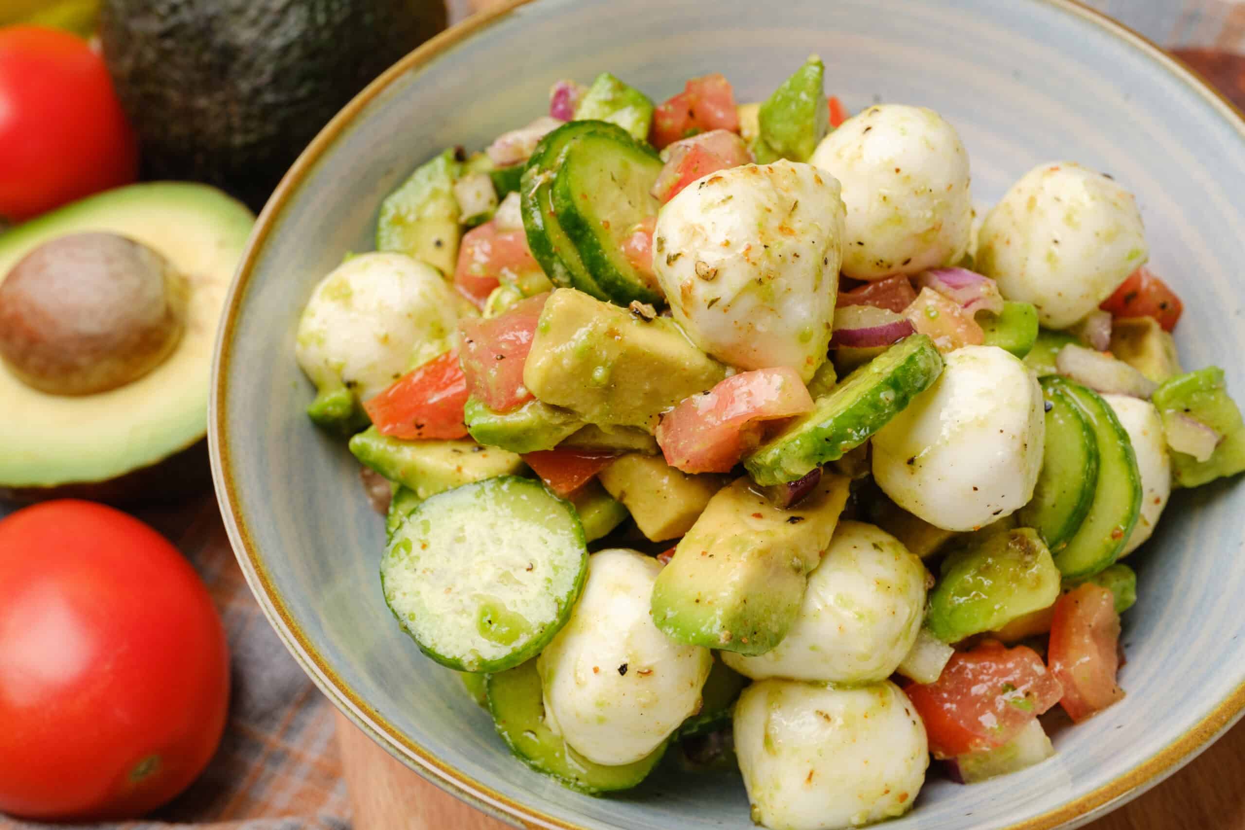 Fresh tomato, cucumber, and mozzarella salad with avocado and herbs in a ceramic bowl, perfect for healthy eating and summer recipes.