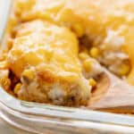 Creamy cheesy casserole with melted cheese, corn, and seasoned meat, served in a glass dish with a wooden spoon, perfect for comfort food recipes.