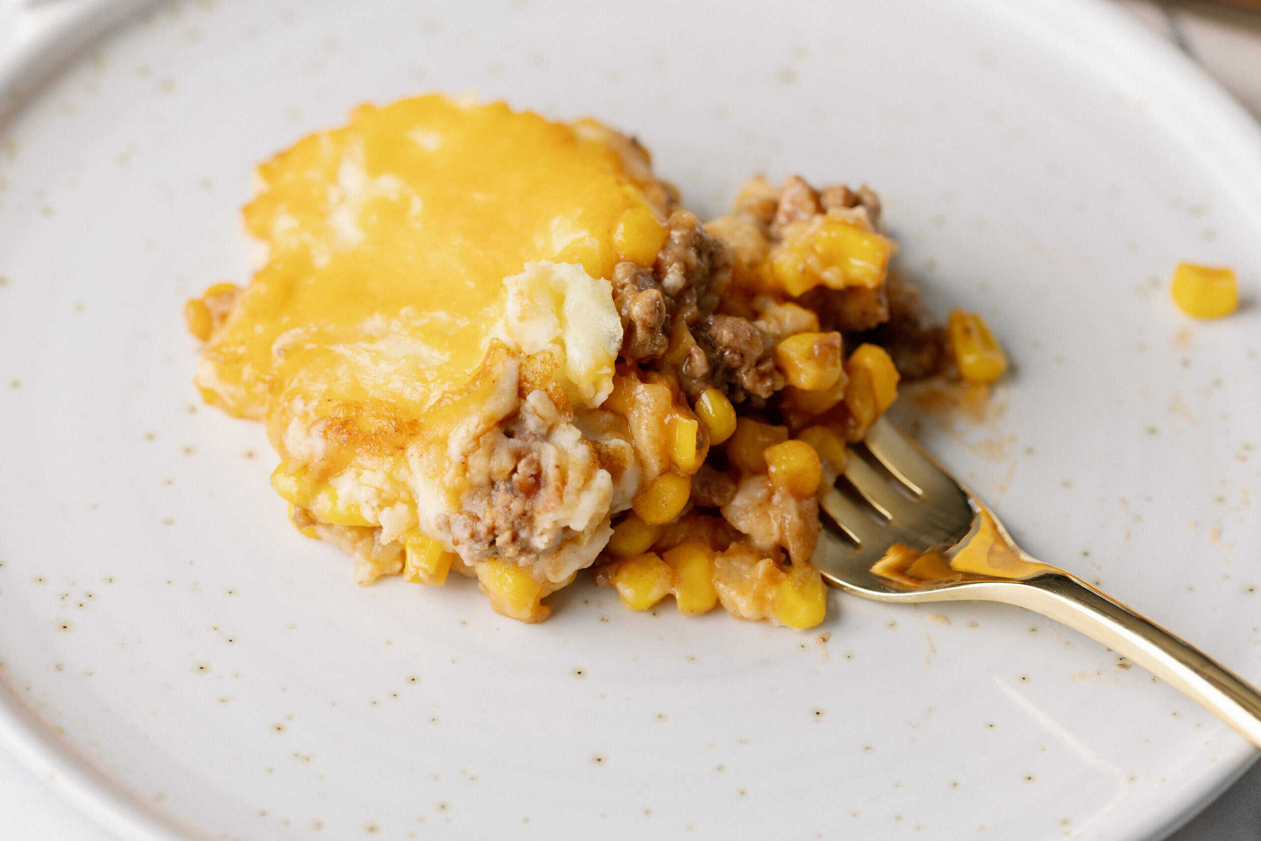 Creamy ground beef and corn casserole with melted cheese served on a white plate.