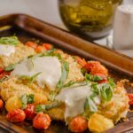 Spanakopita with cherry tomatoes and fresh herbs on a rustic baking tray.