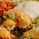 Golden fried fish fillet with creamy white sauce, served with roasted cherry tomatoes and fresh basil leaves on a rustic wooden platter. Perfect for seafood lovers seeking delicious, crispy fish recipes.