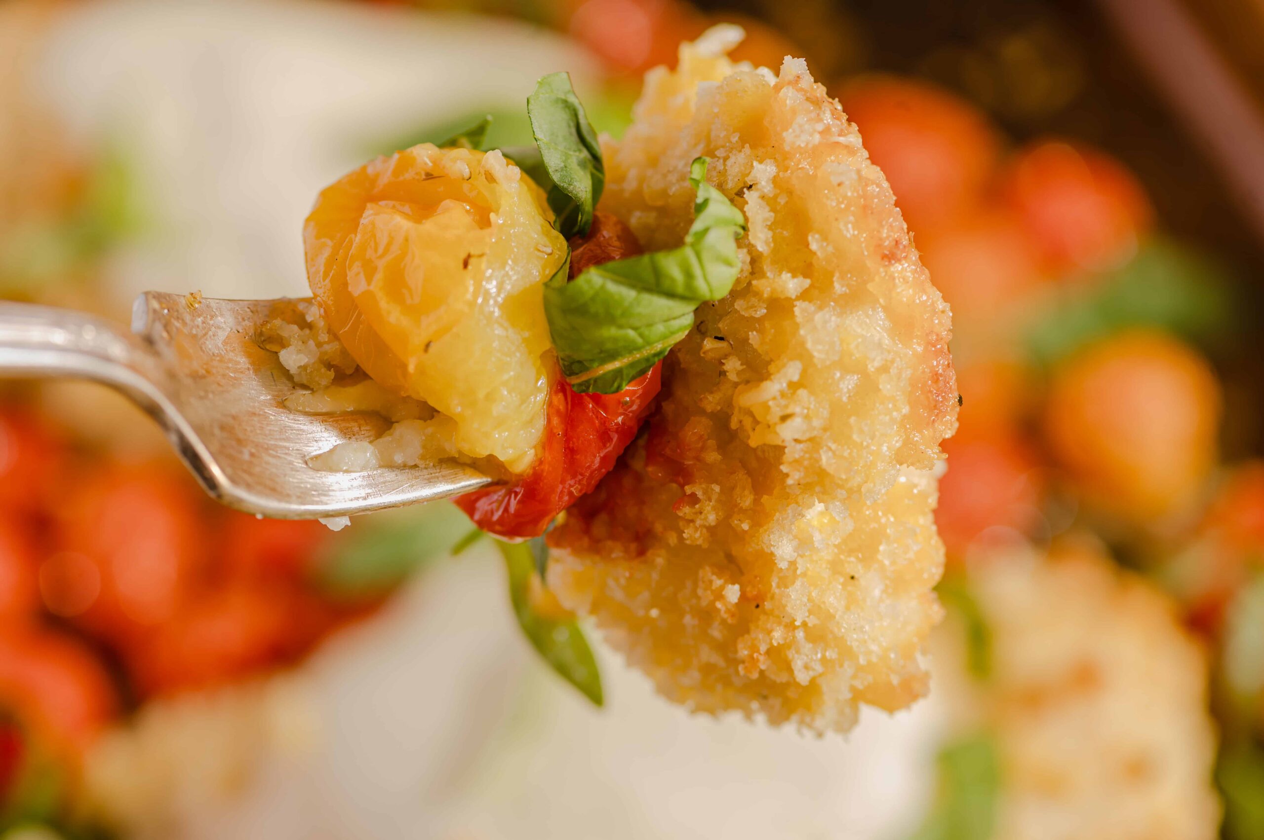 Golden fried chicken tender with a topping of fresh tomato, basil leaf, and melted cheese, served on a fork. Perfect for a savory snack or appetizer with crispy and juicy textures.