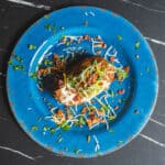 Savory loaded burrito on a vibrant blue plate, topped with shredded cheese, sour cream, bacon bits, chopped green onions, and fresh herbs, served on a dark textured background.