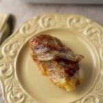 Savoury baked chicken breast topped with melted cheese and tomato sauce served on an elegant cream-colored ornate plate.