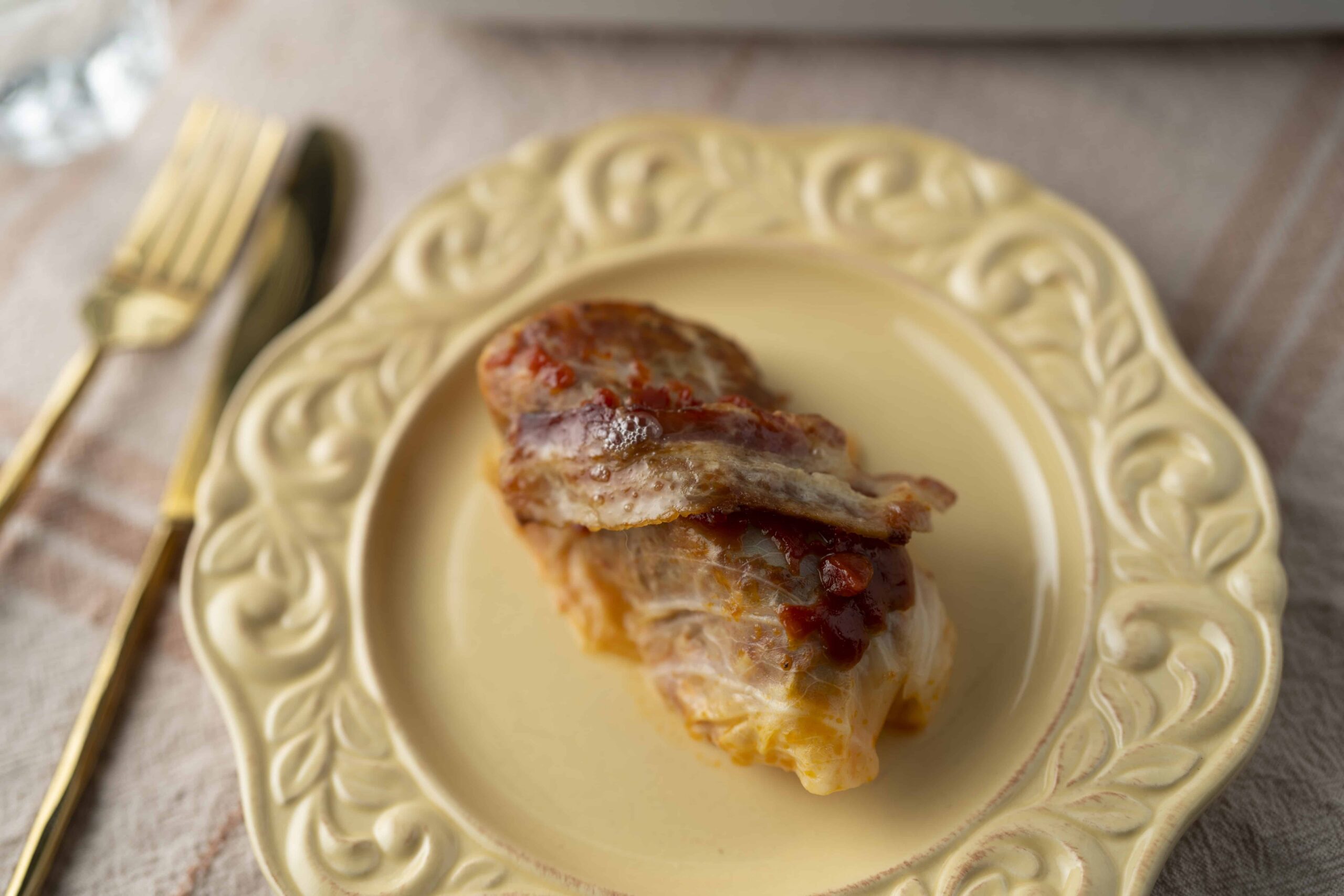Savoury baked chicken breast topped with melted cheese and tomato sauce served on an elegant cream-colored ornate plate.