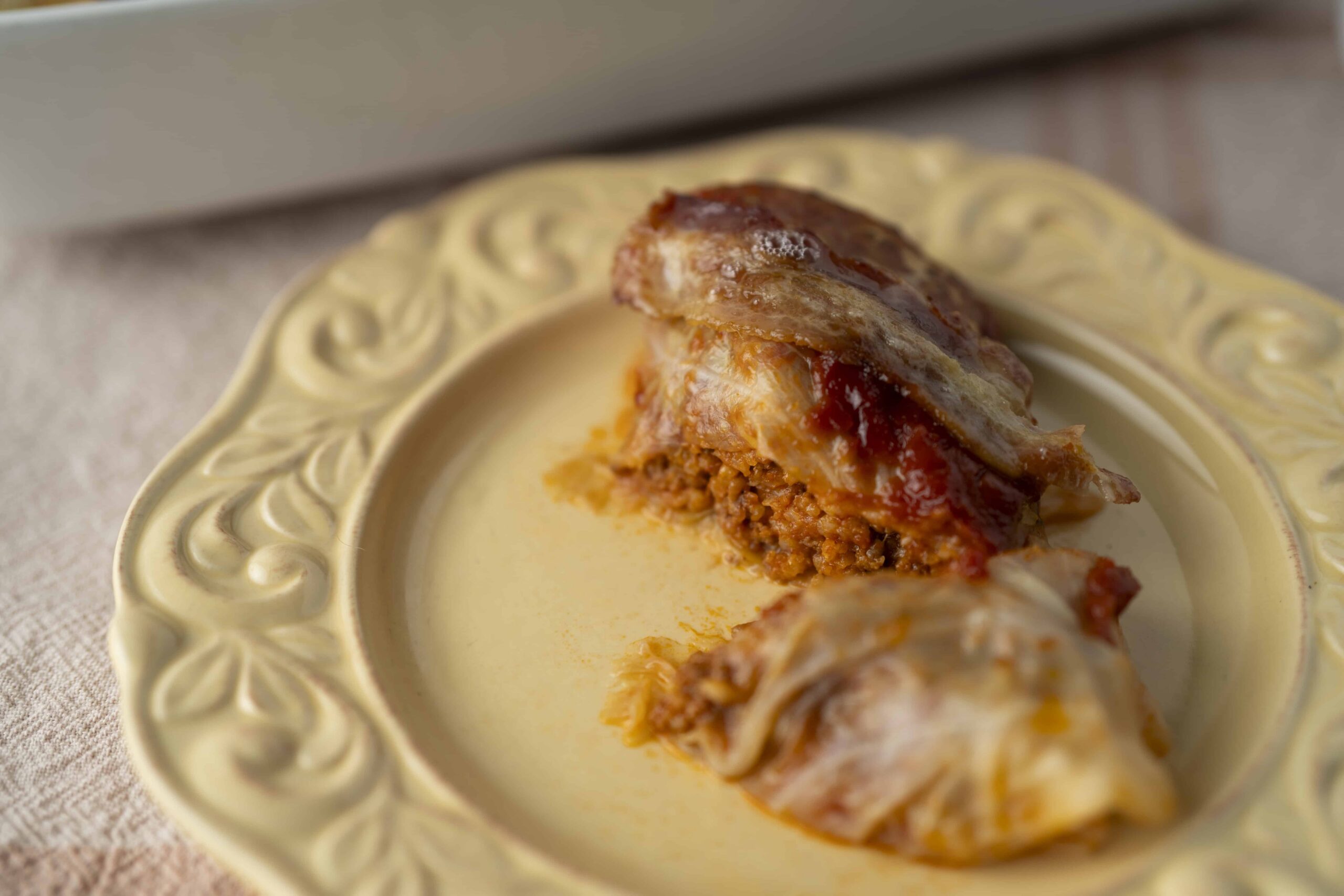 Slow cooker stuffed cabbage rolls with ground meat and tomato sauce served on an ornate ceramic plate.
