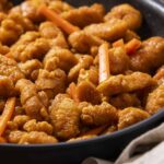 Crispy sweet and sour chicken stir-fry with orange sauce and fresh vegetables, served in a black skillet for a delicious Chinese-inspired meal.