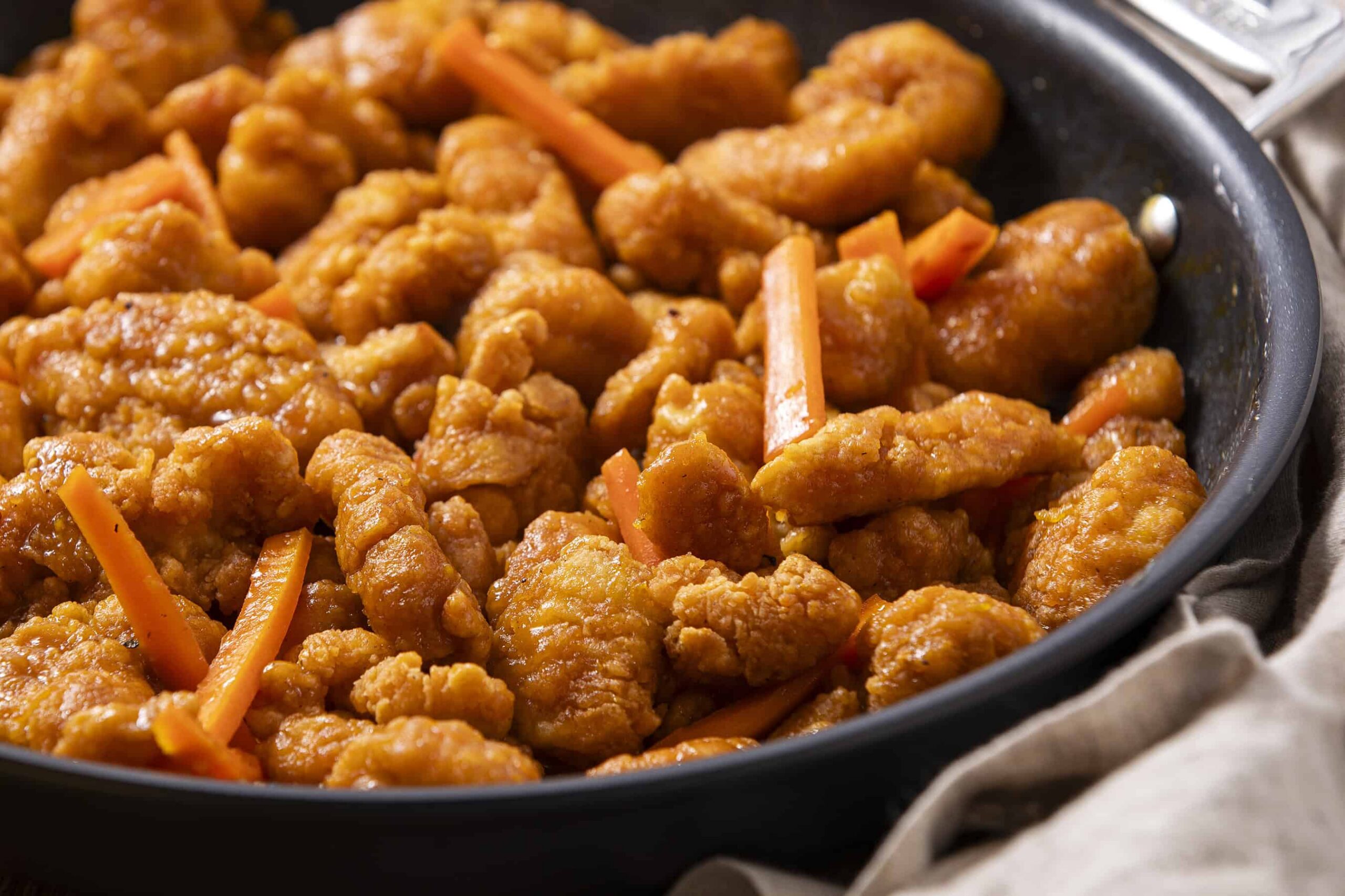 Crispy sweet and sour chicken stir-fry with orange sauce and fresh vegetables, served in a black skillet for a delicious Chinese-inspired meal.