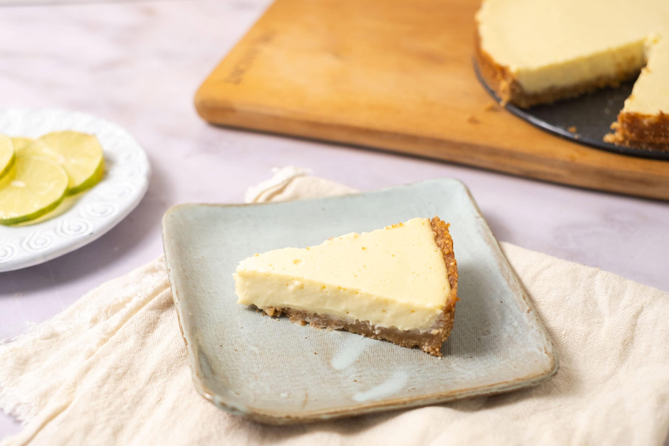 Creamy cheesecake slice on a light green plate, with a graham cracker crust and smooth, rich topping, served with fresh lemon slices in the background. Perfect dessert for cheesecake lovers and gatherings.
