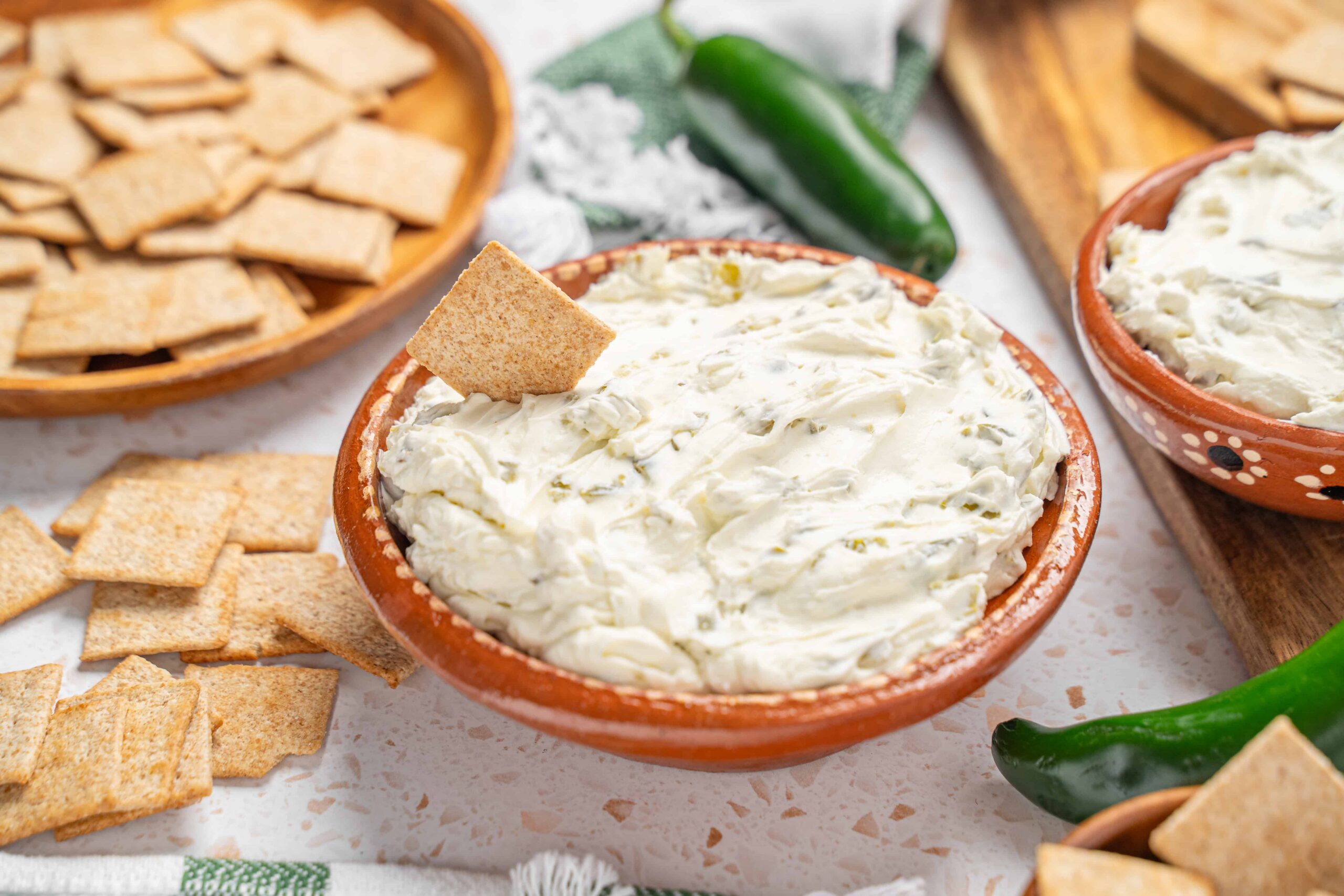 Cream cheese dip with jalapeno peppers and crispy crackers for snack or party platter. Fresh jalapenos adds a spicy kick to creamy, rich cheese spread, perfect for dipping or spreading on bread.
