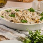 Savory creamy mushroom and chicken casserole garnished with fresh parsley in a white baking dish. Perfect comfort food dish with tender mushrooms and chicken in a rich sauce, served for family meals or special occasions.