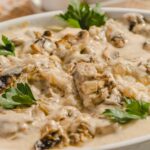 Creamy mushroom chicken casserole with fresh parsley garnish in a white serving dish, featuring tender chicken, sautéed mushrooms, and rich creamy sauce, perfect for hearty comfort food.
