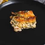 Baked vegetable lasagna square with cheese on a black plate, garnished with herbs and golden crust, perfect for family dinner or comfort food craving.
