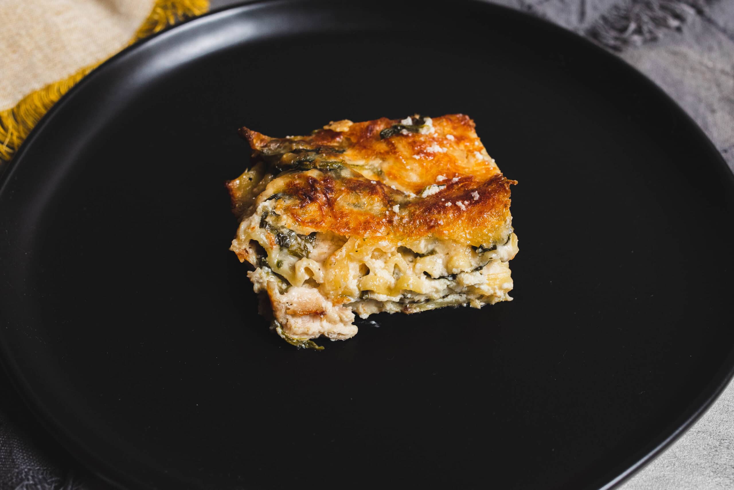 Baked vegetable lasagna square with cheese on a black plate, garnished with herbs and golden crust, perfect for family dinner or comfort food craving.
