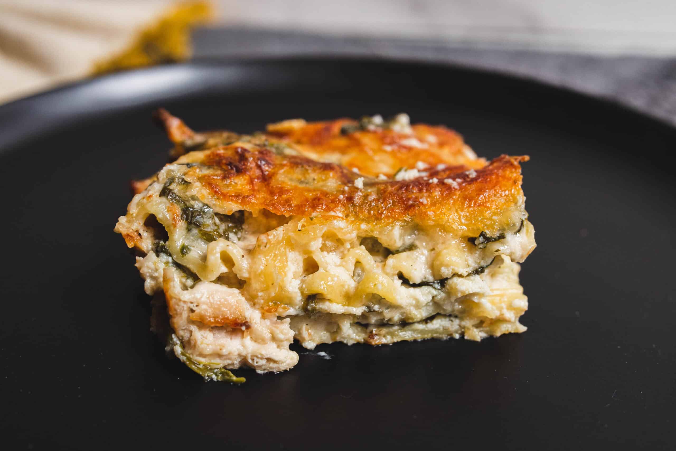 Savory spinach and cheese lasagna with crispy golden top on black plate, homemade Italian casserole, cheesy layered pasta dish, close-up of fresh baked lasagna, hearty comfort food recipe photo.