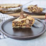 Creamy Nutella cookie dough cheesecake topped with melted chocolate on a dark plate.