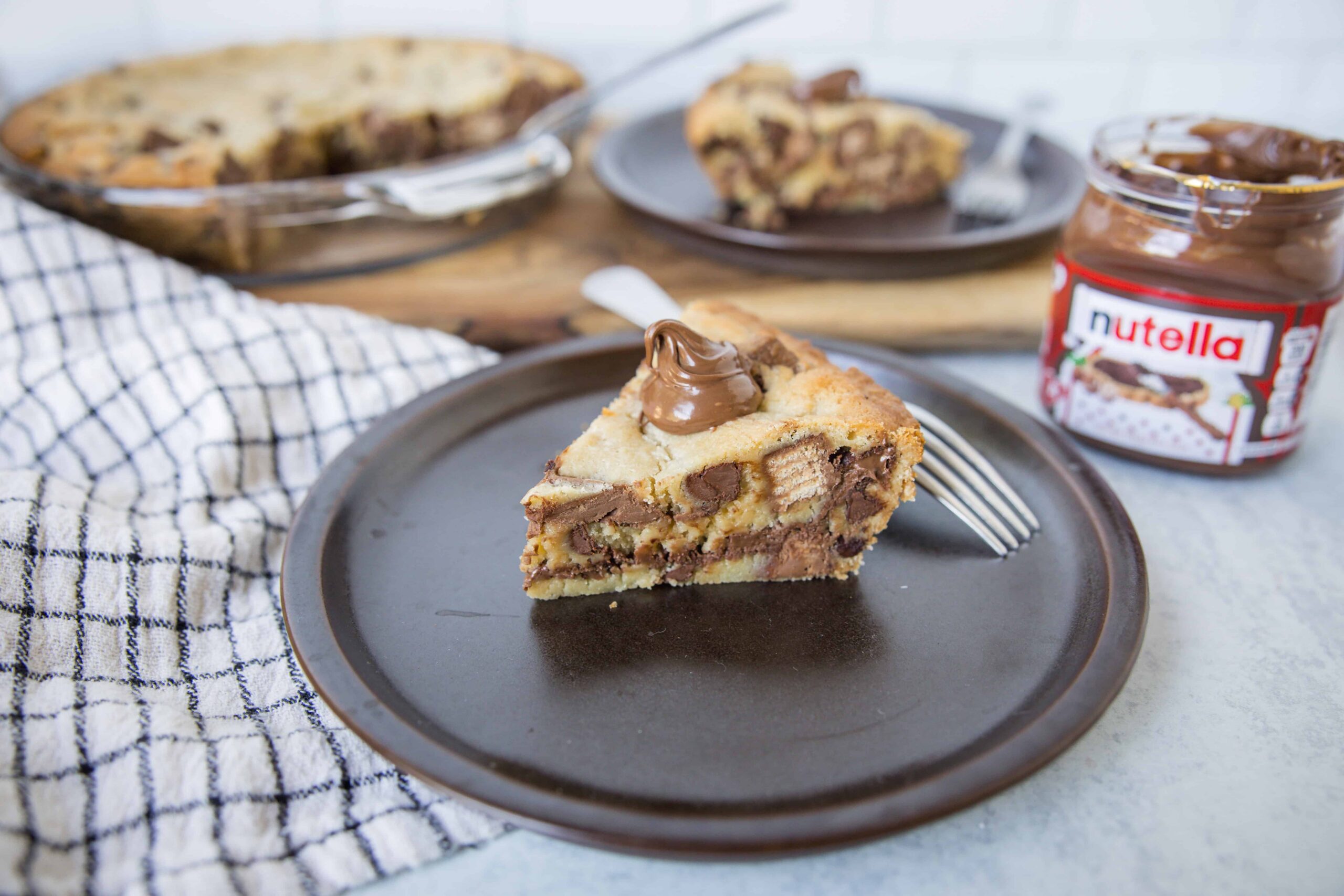 Cream cheese and chocolate chip cookie dough cheesecake topped with Nutella on a dark plate.