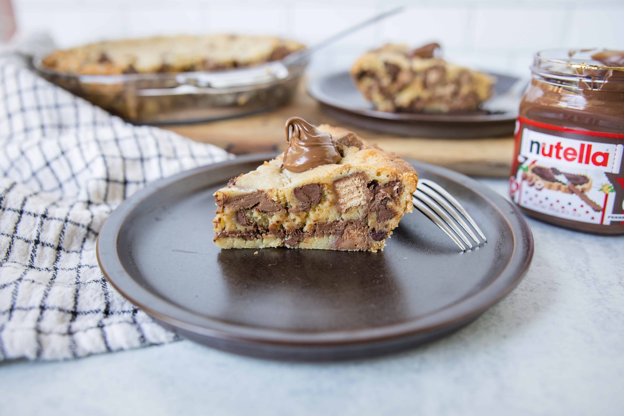 Creamy Nutella cookie dough cheesecake topped with melted chocolate on a dark plate.