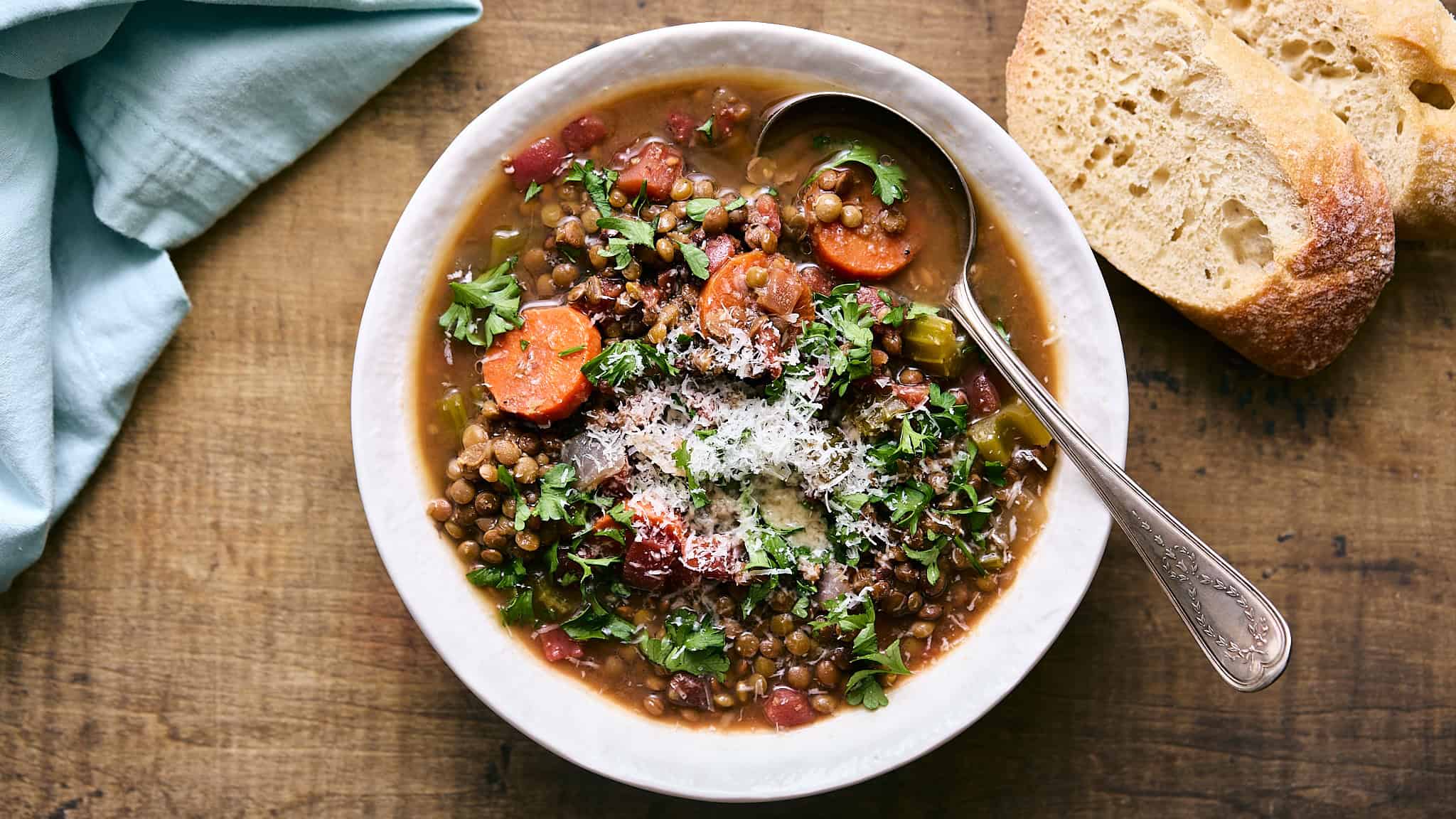 A bowl of hearty lentil vegetable soup garnished with fresh herbs, served with crusty bread on a rustic wooden table.