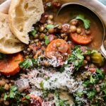 Savory lentil vegetable soup with carrots, celery, fresh herbs, and grated cheese, served with toasted bread slices in a white bowl on rustic wooden background.