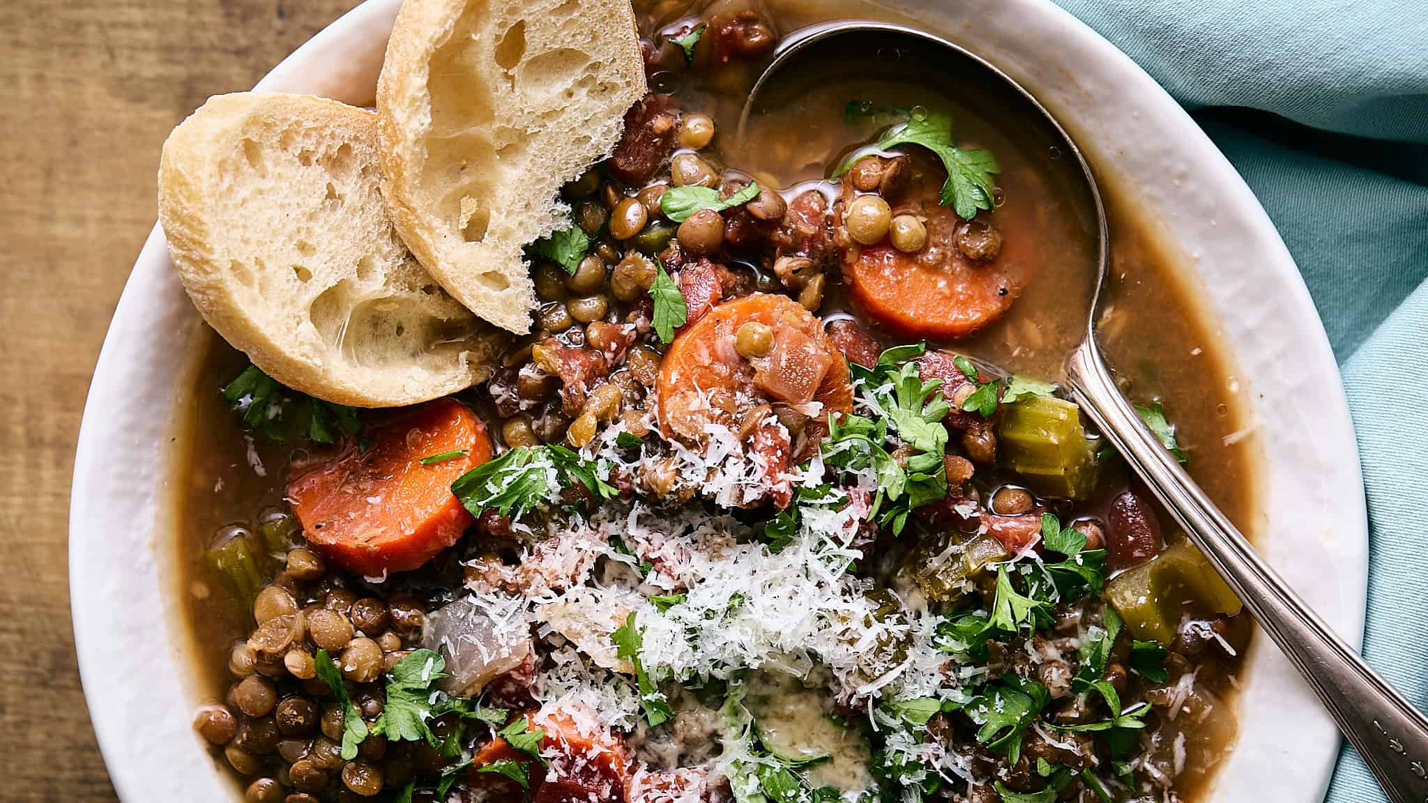 Savory lentil vegetable soup with carrots, celery, fresh herbs, and grated cheese, served with toasted bread slices in a white bowl on rustic wooden background.