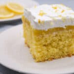 Lemon cake with layers of lemon filling topped with whipped cream and lemon zest, served on a white plate. Perfect for lemon lovers and dessert enthusiasts.