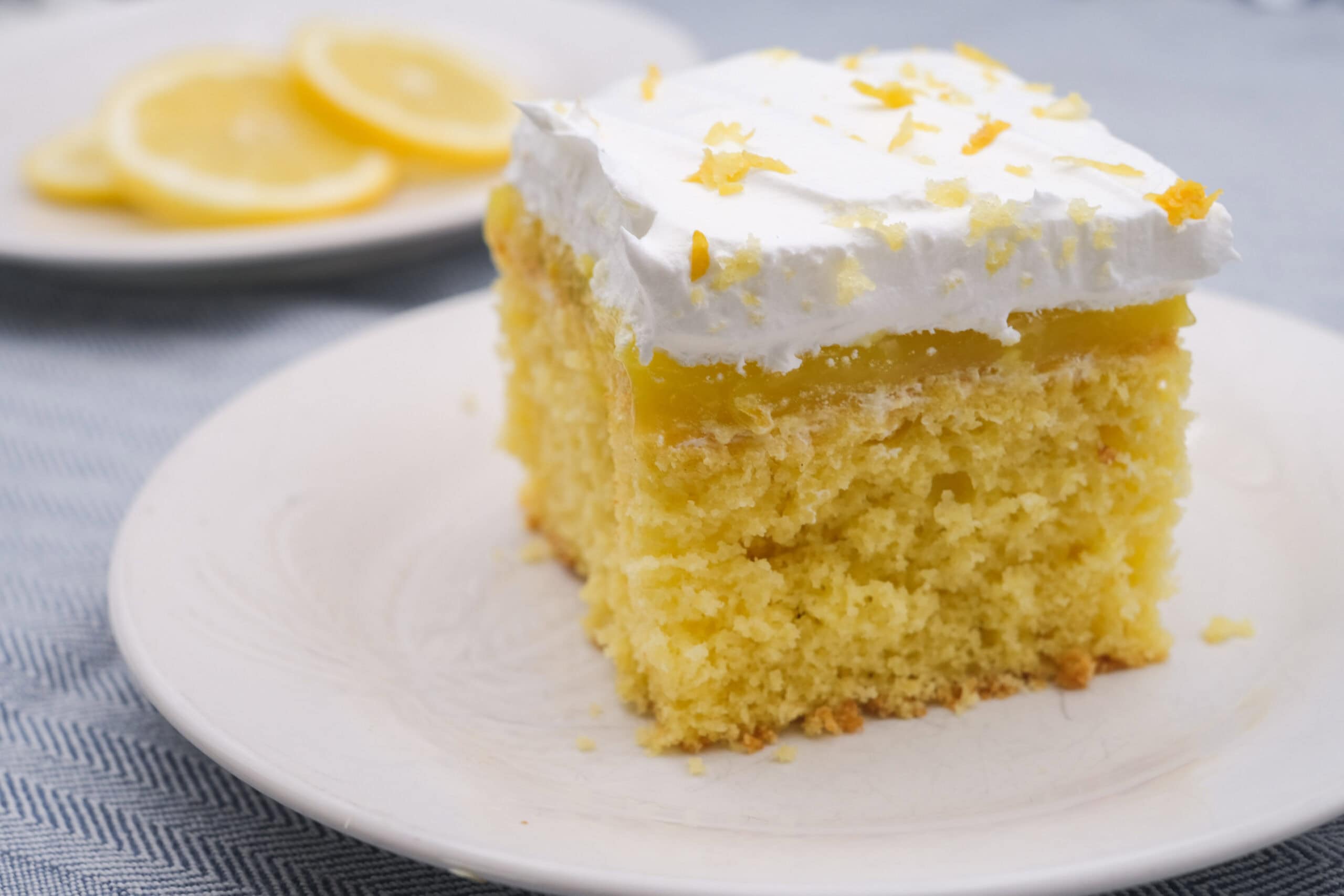 Lemon cake with layers of lemon filling topped with whipped cream and lemon zest, served on a white plate. Perfect for lemon lovers and dessert enthusiasts.
