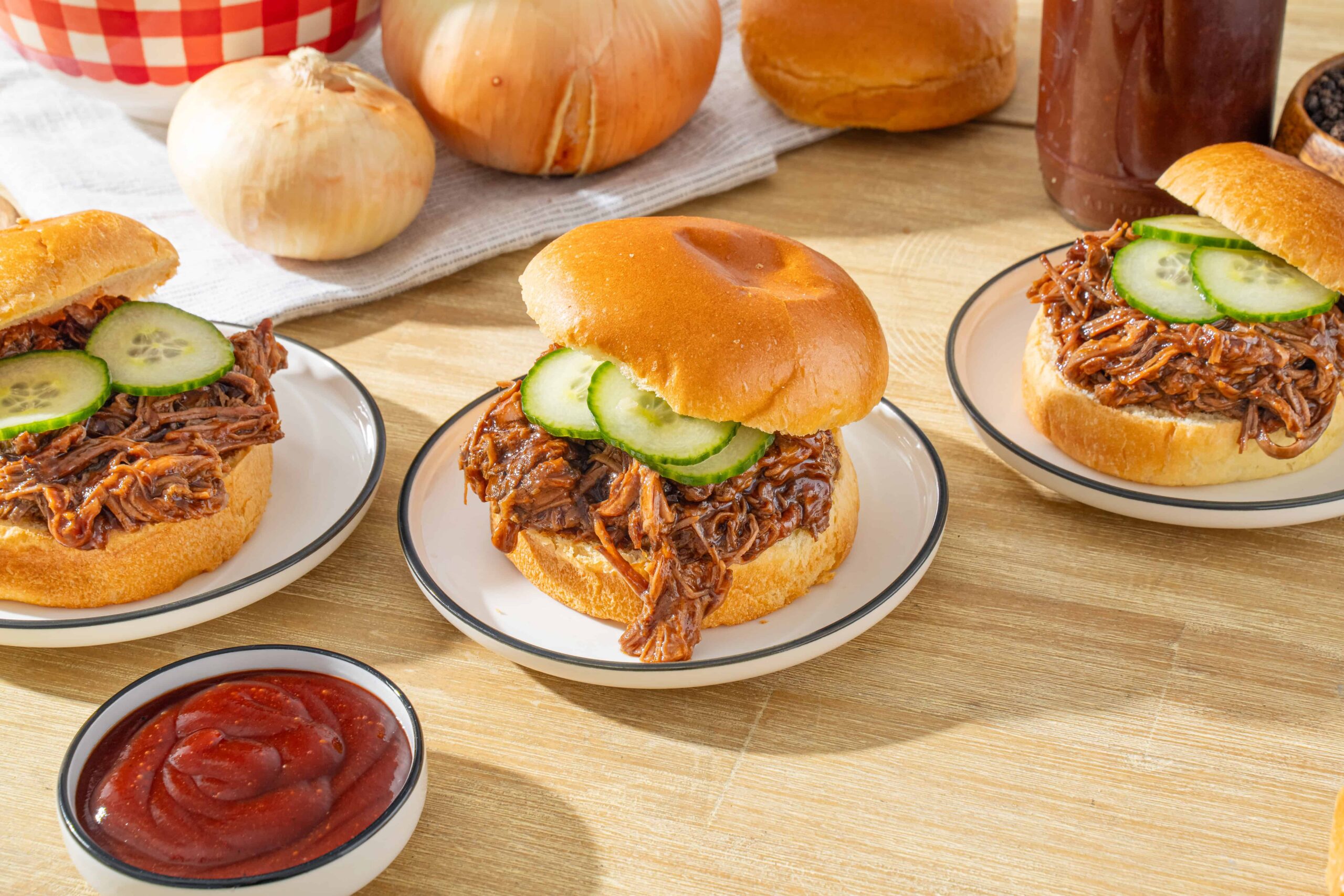 Tender shredded beef barbecue sandwiches on soft buns with fresh cucumber slices, served with ketchup, perfect for a classic bbq meal.