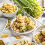 Creamy broccoli and chicken casserole topped with cheese on a white plate, with pasta, fresh celery stalks, peas, butter, and utensils on a rustic wooden table.