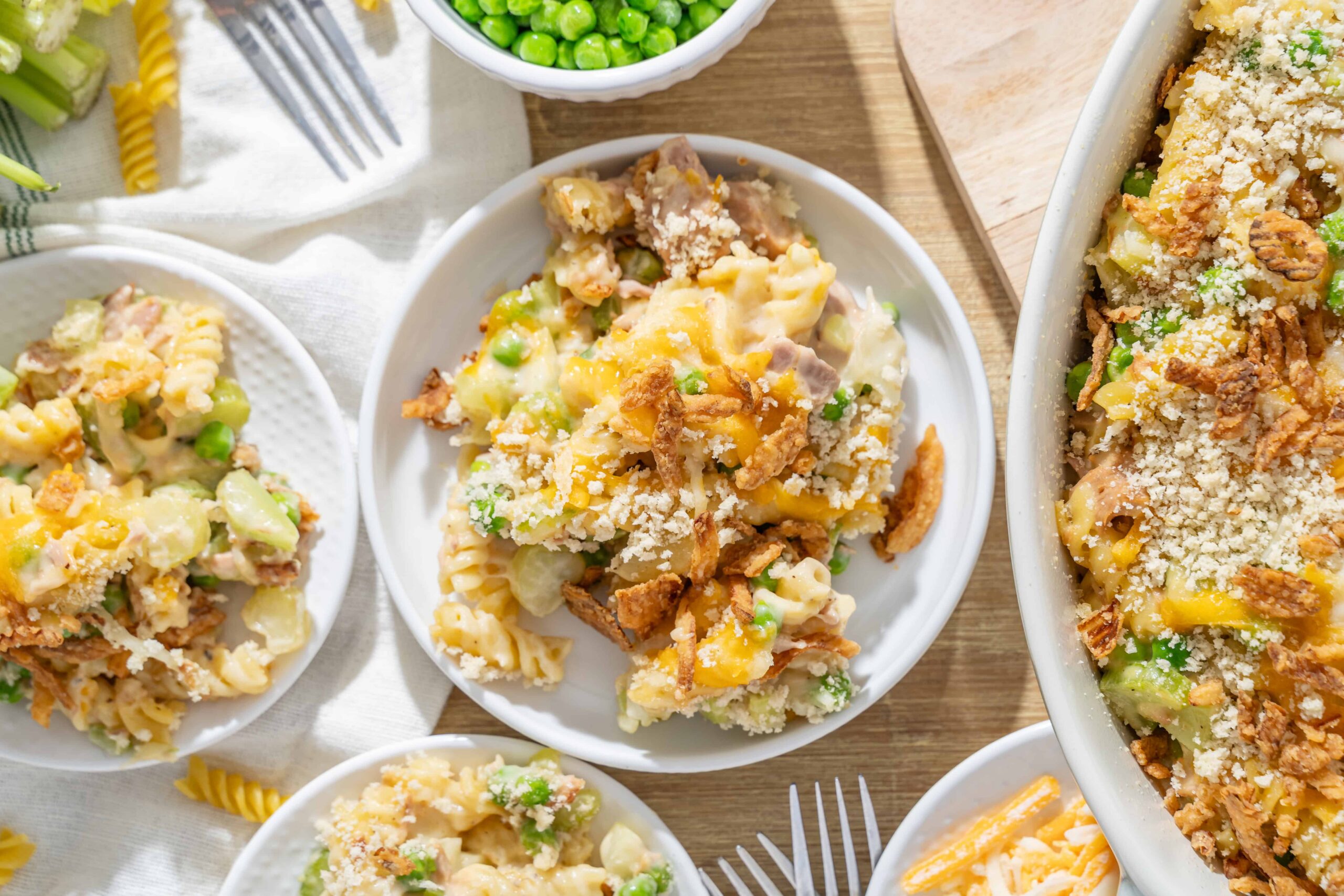 Creamy casserole with pasta, peas, shredded cheese, and crispy fried onions on top, served on white plates for a comforting family meal.