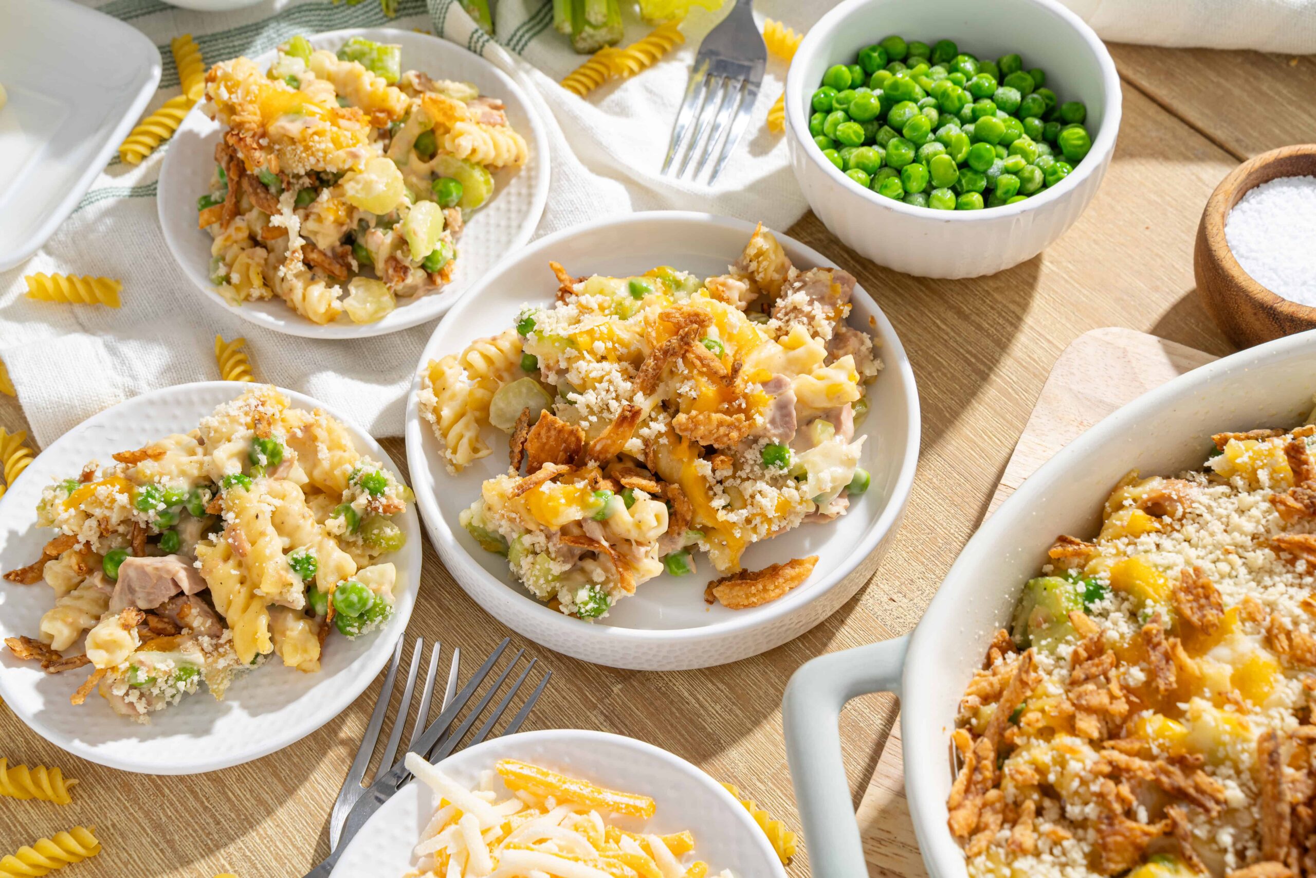 Creamy chicken and vegetable casserole with cheese, served in white bowls with green peas and shredded cheese toppings on a wooden table.