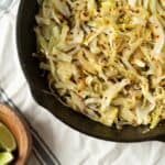 Sauteed cabbage with red pepper flakes in a black skillet, served with lime wedges on the side, perfect for healthy side dish or vegetarian meal.
