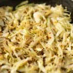 Sautéed shredded cabbage with red pepper flakes in a black skillet, ready for serving or further cooking. Perfect for healthy recipes and vegetable side dishes.