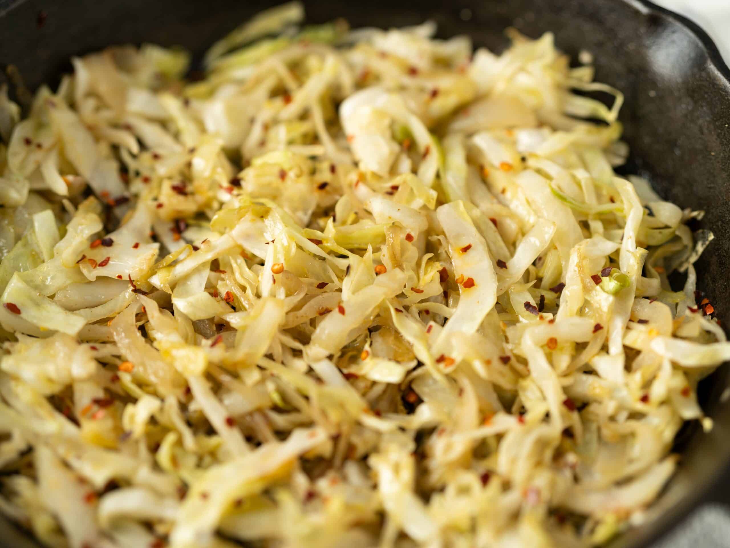 Sautéed shredded cabbage with red pepper flakes in a black skillet, ready for serving or further cooking. Perfect for healthy recipes and vegetable side dishes.